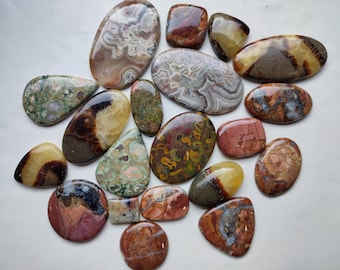 May include: Assortment of 18 polished agate cabochons in various colors and patterns, including brown, green, yellow, red, and white. The cabochons are all different shapes and sizes, and they are arranged in a random pattern on a white surface.