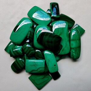 May include: A collection of green malachite cabochons, some with swirling patterns, in various sizes and shapes.