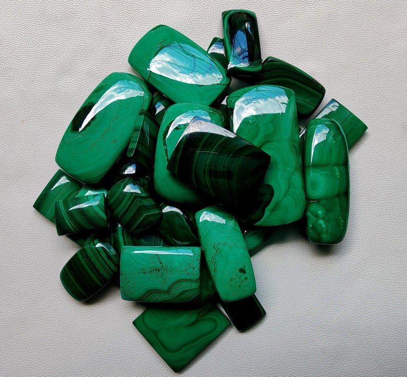 May include: A collection of green malachite cabochons, some with swirling patterns, in various sizes and shapes.