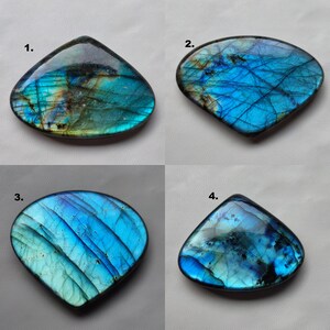 May include: Four iridescent labradorite gemstone cabochons in various shades of blue and green. The stones are shaped like teardrops and have a smooth, polished surface.