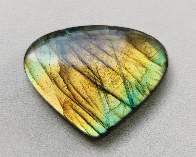May include: A triangular, iridescent labradorite gemstone with a yellow, green, and blue color pattern.