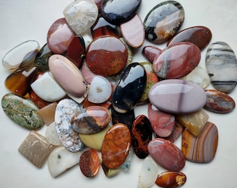 May include: A collection of colorful, polished agate stones in various shapes and sizes. The stones have a variety of patterns and colors, including red, brown, white, black, and green.