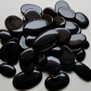 May include: A pile of smooth, black oval-shaped stones. The stones are polished and have a glossy finish.