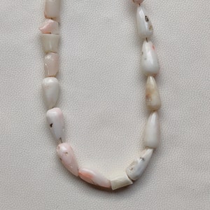 May include: A necklace made of pink and white shell beads. The beads are all teardrop shaped and have a natural, organic look.