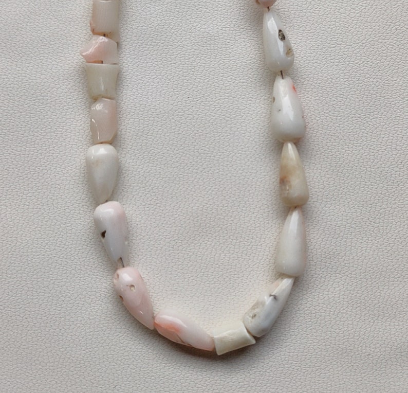May include: A necklace made of pink and white shell beads. The beads are all teardrop shaped and have a natural, organic look.