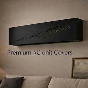 May include: A black rectangular AC unit cover with a perforated design, mounted on a beige wall. The text "Premium AC unit Covers" is displayed below the cover. The cover is above a sofa with grey cushions.
