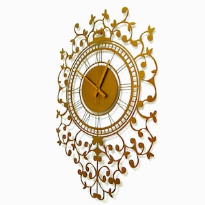 May include: A gold-colored metal wall clock with a decorative floral design. The clock face has Roman numerals and a gold-colored frame.