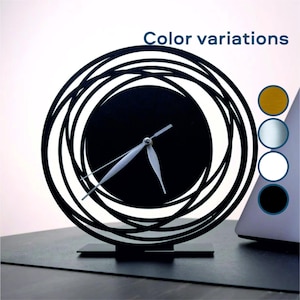 Può includere: Orologio astratto bianco e nero con un design circolare e lancette bianche. L'orologio è su un supporto nero e si trova su un tavolo.