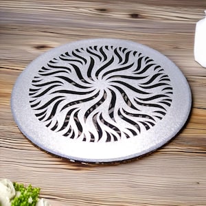 Op de afbeelding: Een ronde zilveren dienblad met een zwart swirl-ontwerp dat uit het midden is geknipt. Het dienblad ligt op een houten oppervlak.
