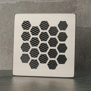 Puede incluir: Una rejilla de ventilación de metal blanco con un patrón de panal negro.