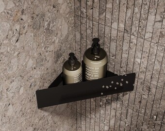 Puede incluir: Una estantería de esquina negra sostiene dos botellas marrones con bombas negras. Las botellas tienen texto blanco que dice "French Oak" y "Purple Iris". La estantería está montada en una pared de azulejos grises, creando una estética de baño moderna.