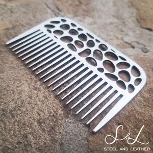 May include: A silver comb with a unique, patterned design. The comb has a rounded shape and a textured surface. The comb is made of metal and has a sleek, modern look.