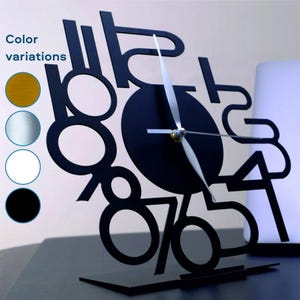 May include: Black metal desk clock with numbers 1 through 12 displayed in a unique, abstract design. The clock has a black face and silver hands.
