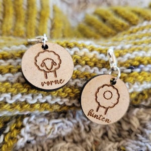 Könnte beinhalten: Zwei hölzerne Maschenmarkierer mit Schafmotiven. Ein Marker sagt "vorne" und der andere sagt "hinten".