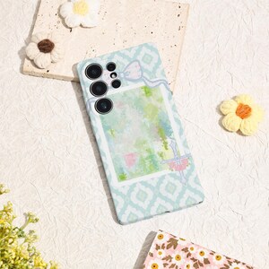 May include: A light blue phone case with a white geometric pattern and a watercolor design. The case features a bow and floral accents. The phone case has a camera module with multiple lenses.