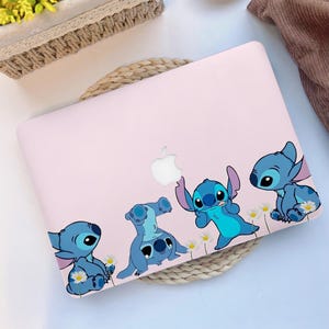 Può includere: Una custodia per laptop rosa chiaro con quattro personaggi dei cartoni animati blu con grandi orecchie e grandi occhi. I personaggi sono disposti lungo il bordo inferiore, con piccoli fiori bianchi. Il logo Apple è visibile.