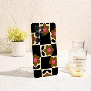 May include: A black and white checkered phone case with a floral pattern. The flowers are brown with pink centers. The case has a camera cutout and is designed for a smartphone.