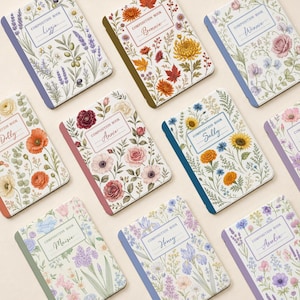 Puede incluir: Una colección de ocho cuadernos de composición con portadas blancas que presentan diversas ilustraciones botánicas de flores y follaje. Cada cuaderno tiene una etiqueta rectangular con el texto COMPOSITION BOOK y un nombre en letra cursiva.