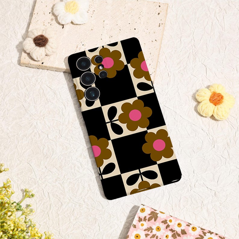 May include: A black and white checkered phone case with a retro floral pattern. The case features brown flowers with pink centers. The phone case has a camera array on the upper left side.