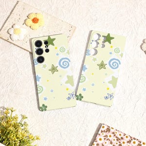 May include: Two light green phone cases with a repeating pattern of stars, swirls, and small flowers in blue, green, and yellow. The cases have cutouts for the phone's camera and buttons. Decorative flowers are in the background.