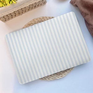 May include: A rectangular laptop skin featuring a pattern of vertical light blue and white stripes. The skin is resting on a woven placemat. The overall aesthetic is clean and minimalist, suitable for a variety of styles.