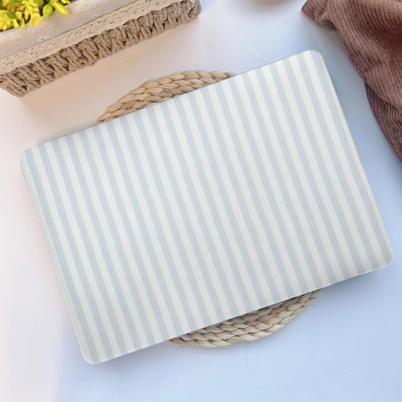 May include: A rectangular laptop skin featuring a pattern of vertical light blue and white stripes. The skin is resting on a woven placemat. The overall aesthetic is clean and minimalist, suitable for a variety of styles.
