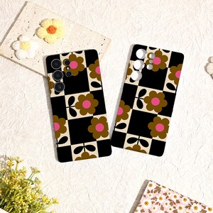 May include: Two phone cases with a retro floral design. The cases feature a black and cream checkerboard pattern with brown and pink flowers. The cases are lying on a white surface with decorative flowers.
