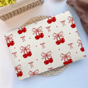May include: A white laptop skin with a repeating pattern of red cherries with bows. The cherries are outlined in black and the bows are white.