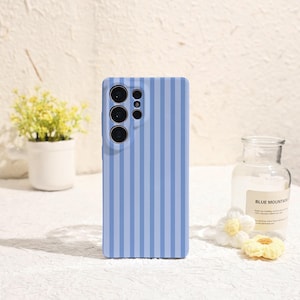 May include: A rectangular smartphone case featuring a vertical striped pattern in alternating shades of light blue and periwinkle. The case includes a cutout section for a multi-lens camera array on the upper left side, maintaining a flat surface.