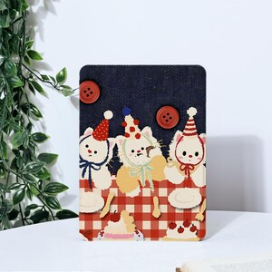 May include: Three white cartoon cats wearing party hats and sitting at a red and white checkered picnic table. The cats are holding plates with cherries and cakes. The background is a dark blue with white stars.