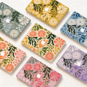 May include: Six rectangular laptop cases featuring floral patterns in various colour palettes including yellow, blue, green, pink, and lavender. Each case displays a central cutout for an Apple logo and is decorated with stylised flowers and leaves.