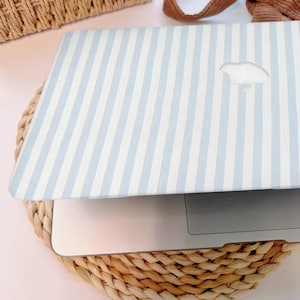 May include: A laptop case with a light blue and white striped pattern. The case has a cutout for the Apple logo and is resting on a woven, circular placemat. The case is open, revealing the laptop's keyboard.