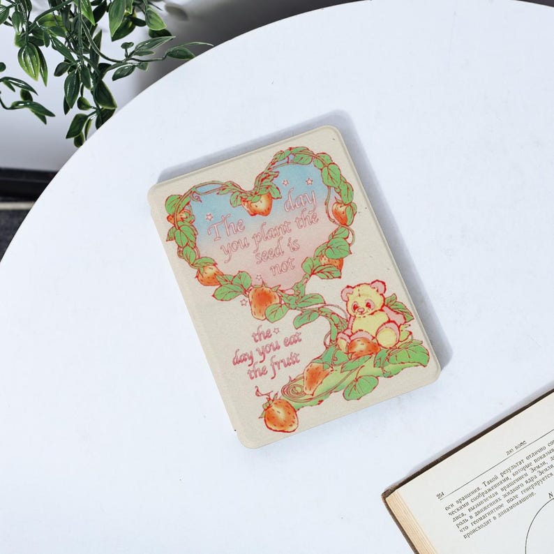 May include: A light brown card with a heart-shaped design featuring a cartoon bear and strawberries. The card has the text "The day you plant the seed is not the day you eat the fruit."