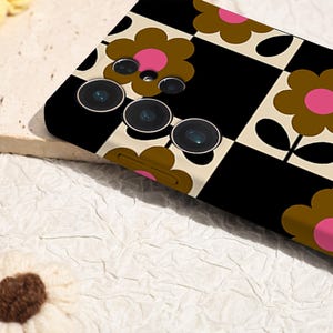 May include: A black and white checkered phone case with brown and pink flower designs. The case has a camera cutout with three lenses.