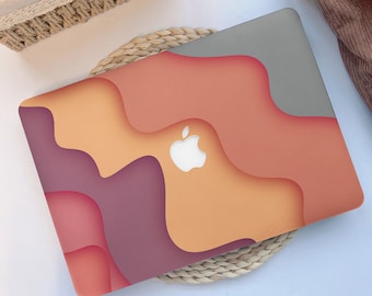 May include: A laptop skin with a colourful abstract design featuring shades of orange, red, and purple. The design resembles layered paper cutouts. The Apple logo is visible in the centre of the skin.