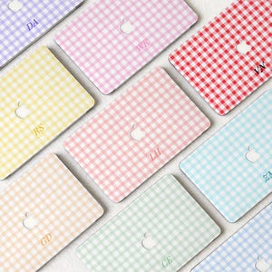 May include: A collection of laptop covers with a gingham pattern in various colors, including red, pink, yellow, and blue. Each cover features a cutout for the Apple logo and personalized initials.