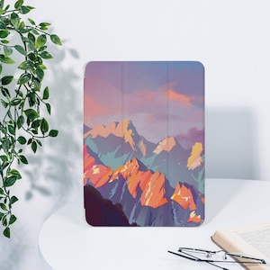 May include: A tablet case with a colorful mountain landscape design. The mountains are painted in shades of purple, orange, and blue against a pink and purple sunset sky.