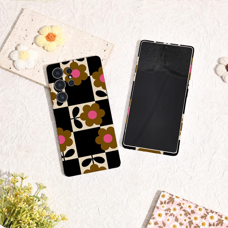 May include: Two phone cases with a retro floral design. One case is on a phone, the other is separate. The design features brown flowers with pink centers on a black and tan checkered background. The phone screens are black.