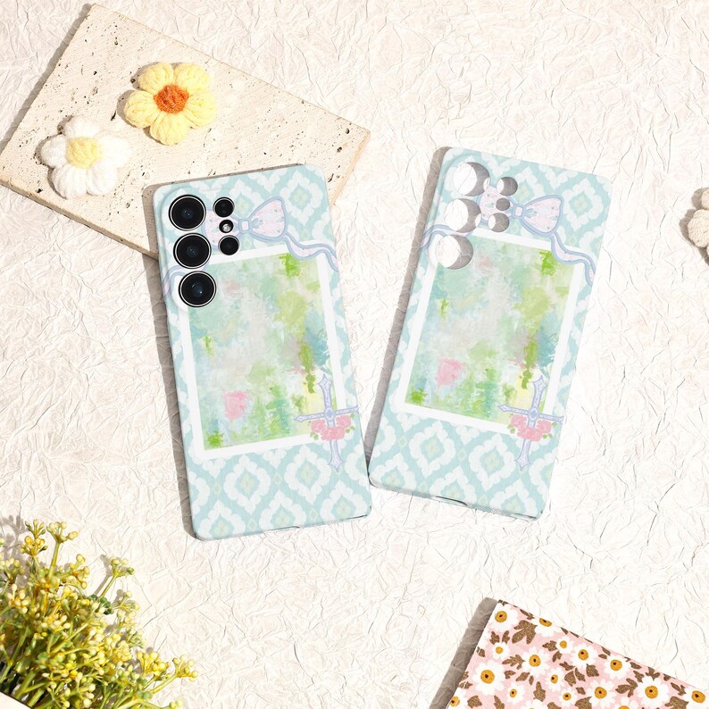 May include: Two phone cases with a light blue geometric pattern and a watercolor design. Each case has a bow and ribbon detail at the top and a floral accent at the bottom. The cases are designed to fit a smartphone.