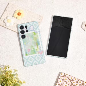May include: A light blue phone case with a white and blue geometric pattern and a watercolor design. The case has a bow and a floral design. A second phone is next to the case.