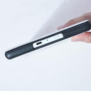 May include: A black phone case with a white phone inside. The case has a cutout for the charging port and a button on the side.