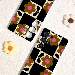 May include: Two phone cases with a retro floral design. The cases feature a black and cream checkerboard pattern with brown and pink flowers. The phone cases are on a white textured surface, with two decorative flower accents.