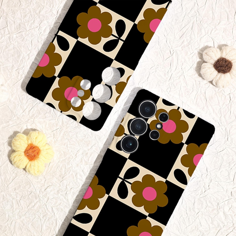 May include: Two phone cases with a retro floral design. The cases feature a black and cream checkerboard pattern with brown and pink flowers. The phone cases are on a white textured surface, with two decorative flower accents.