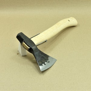 Könnte beinhalten: Eine schwarze und silberne Handaxt mit einem Holzstiel. Die Axt liegt auf einem weißen Block.