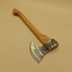 Könnte beinhalten: Eine alte Axt mit einem Holzgriff und einer Metallklinge. Der Griff ist hellbraun, und die Klinge hat eine gebogene Schneide. Die Axt weist Gebrauchsspuren auf. Es ist ein Werkzeug zum Hacken von Holz.