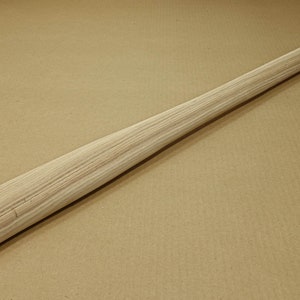 Könnte beinhalten: Ein einfacher Holzgriff für einen Hammer oder ein anderes Werkzeug. Der Griff ist aus hellem Holz mit einer glatten Oberfläche.