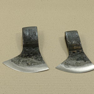 May include: Two small, hand-forged axes with curved blades and wooden handles. The axes are made of metal and have a rustic, aged appearance.