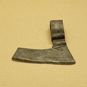 Peut inclure: Une tête de hache vintage forgée à la main avec une lame incurvée et un œillet arrondi. La tête de hache est en métal et présente une patine gris foncé.