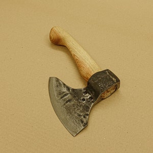 Peut inclure: Une hache forgée à la main avec un manche en bois. La tête de la hache est en acier et possède une lame incurvée. Le manche est en bois clair et a une finition naturelle.