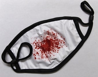 May include: White face mask with a black trim and adjustable ear loops. The mask features a red blood splatter design. The mask is made of a soft, breathable material.